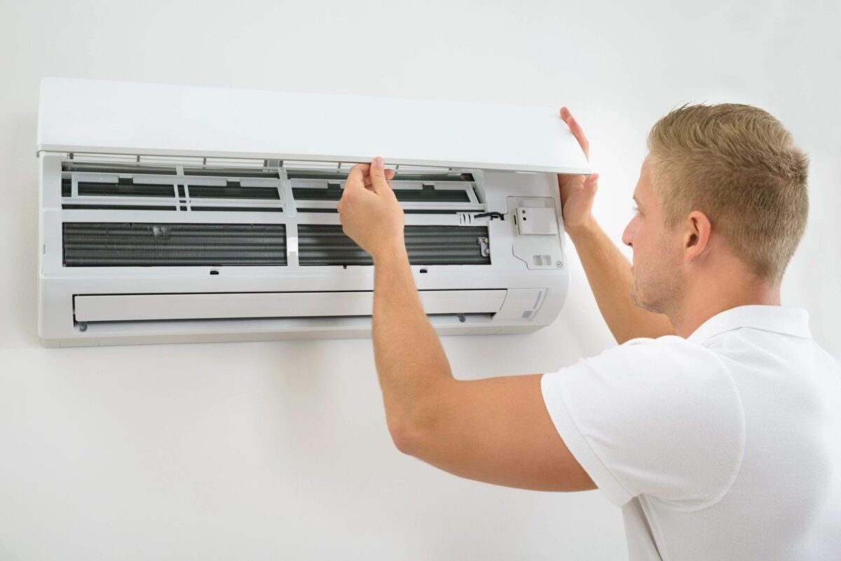 A person in a white shirt adjusts the cover of a wall-mounted air conditioning unit.