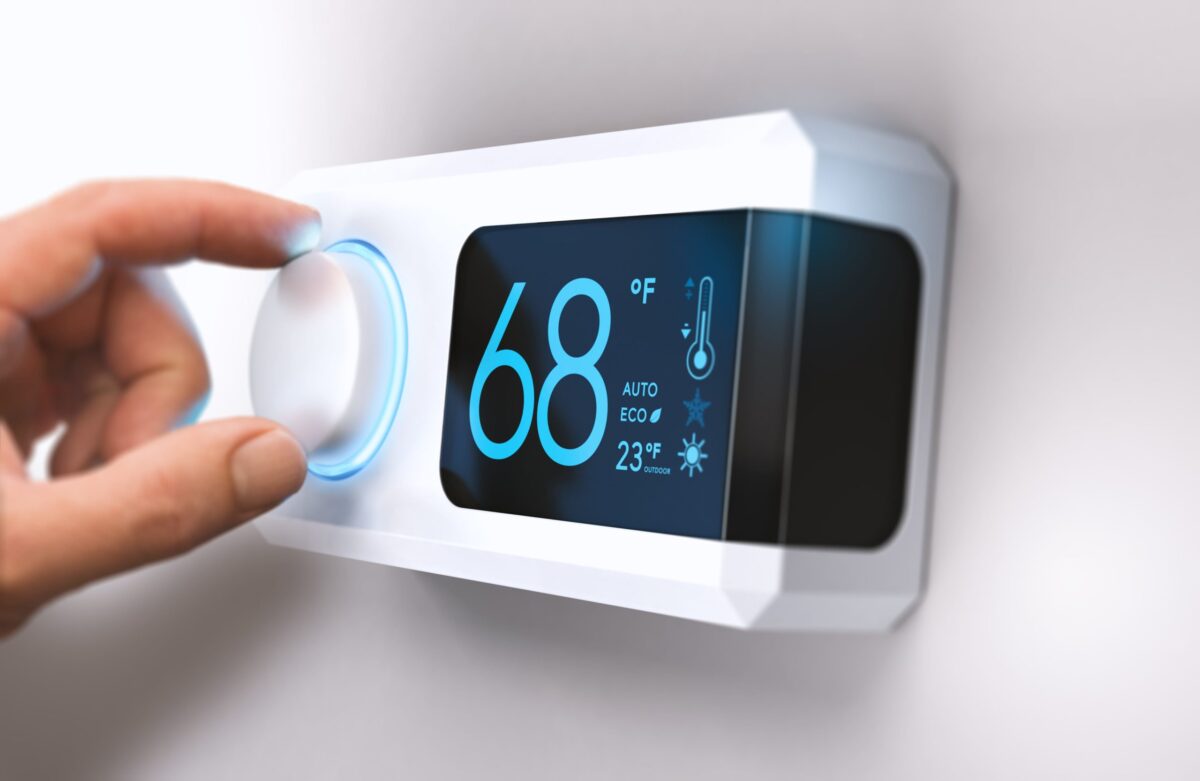 A hand adjusts a modern digital thermostat set to 68°F with options for auto, eco, and a snowflake symbol visible on the screen.