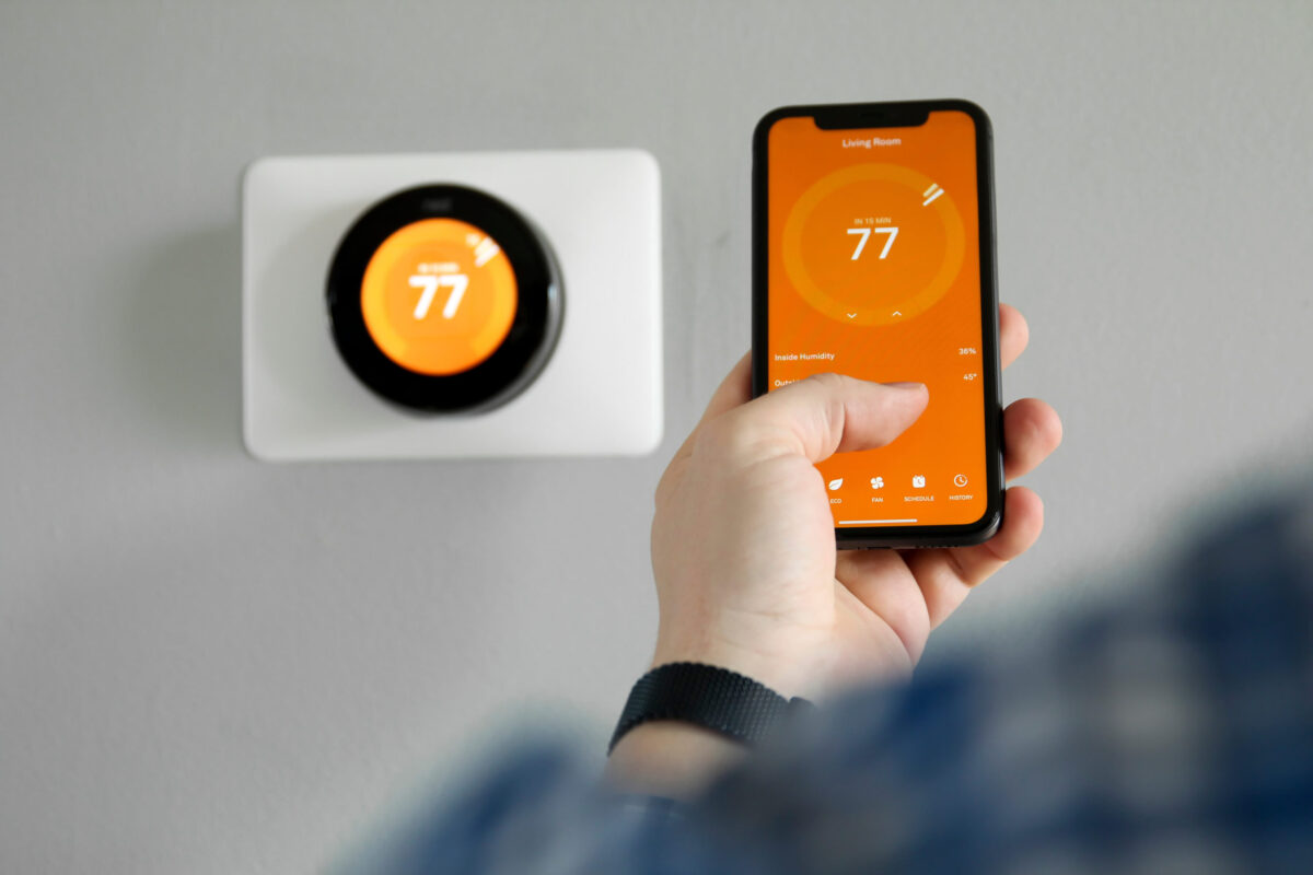 A person adjusts a smart thermostat to 77 degrees using a smartphone app.