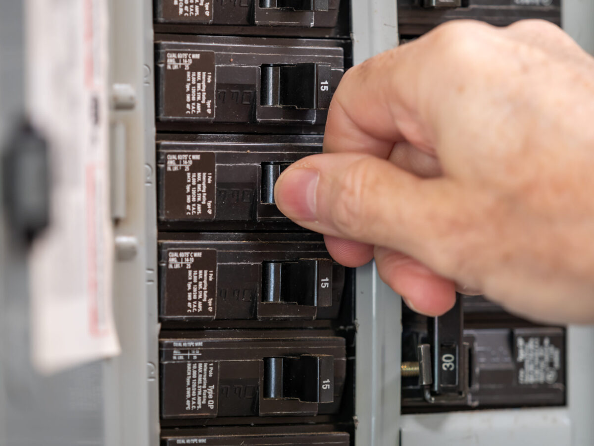 A hand flipping a switch on a circuit breaker panel.