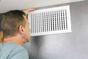 Person inspecting a white air vent on a gray wall.