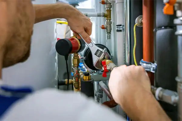 A Person Uses A Wrench To Adjust A Pipe Connected To Plumbing And Heating Equipment.