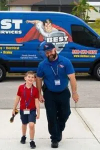 An Adult In A Blue Uniform And A Child In A Red Shirt Stand Smiling In Front Of A Blue Service Van With &Quot;Best Services&Quot; Written On It.